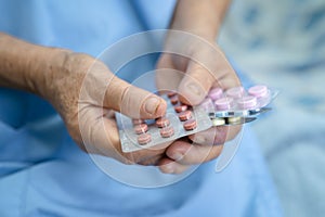 Asian senior or elderly old lady woman patient holding antibiotics capsule pills in blister packaging for treatment infection
