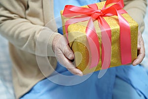 Asian senior or elderly old lady woman patient with Santa Claus helper hat holding gift box in Christmas and new year celebration