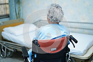 Asian senior or elderly old lady woman patient sitting on wheelchair near bed in nursing hospital ward