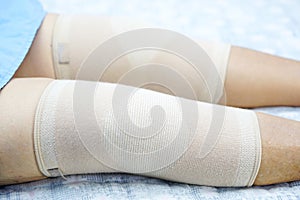 Asian senior or elderly old woman patient with bandage compression knee brace support injury on the bed in nursing hospital