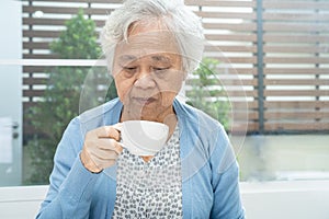 Asian senior or elderly old woman patient holding mug and drinking coffee in the morning at home,  healthy strong medical concept