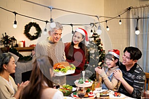 Asian senior father and daughter serving roasted turkey food on dinner table while warm family gathering and clapping hand for