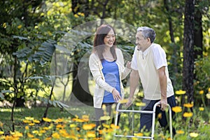 Asian senior father with walker and daughter walking together in the park during summer for light exercise and physical therapy