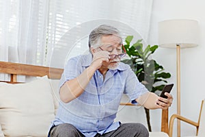 Asian senior fatigue man taking off glasses during using smartphone