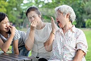 Asian senior grandmother checking breath with her hand,elderly people bad breath,daughter,granddaughter closing her nose,very bad