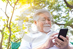 Asian senior man chatting with family by using smart phone, video call, internet wireless at park. His family stay at overseas. Ma