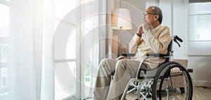 Asian senior man disabled sitting alone in wheelchair looking through window at hospital