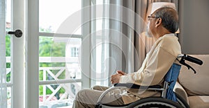 Asian senior man disabled sitting alone in wheelchair looking through window at hospital