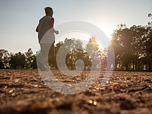 Asian senior man jogging in the park over sunset sky background. Healthy lifestyle and Healthcare concept