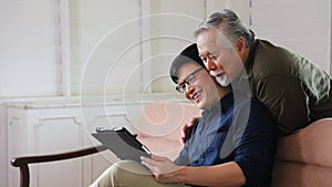 Asian senior man learn how to use digital tablet from his son while sitting on the sofa at retirement home