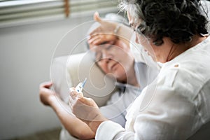 Asian Senior man lying on sofa while his wife holding and looking to thermometer