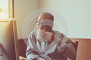 Asian senior man serious and drinking coffee with using computer at home in the morning
