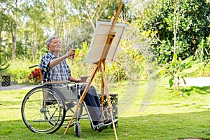 Asian senior man sit on wheelchair and action of aim or point to the area of model for paint the painting outdoor for relax