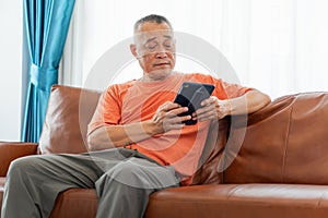 Asian senior man sitting on sofa and using digital tablet in living room