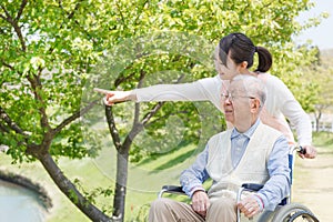 Asian senior man sitting on a wheelchair with caregiver pointing