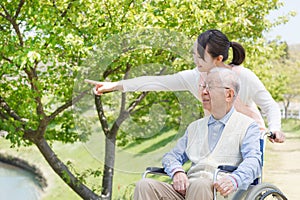 Asian senior man sitting on a wheelchair with caregiver pointing photo