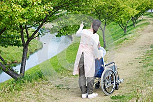 Asian senior man sitting on a wheelchair with caregiver pointing