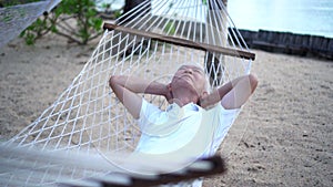 Asian senior man sleeping on hammock at resort beach side