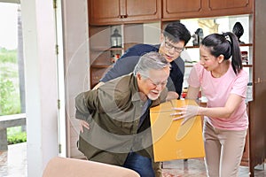 Asian senior man is suffering from back pain while carrying too heavy box while his children is coming to help and taking care of