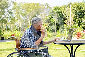 Asian senior man take off the eyeglasses to look more clearly for watching the laptop outdoor in the garden