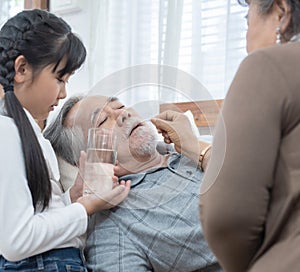 Asian Senior man taking medicines and drinking water while lie on couch at home, health and medicine concept with copy space