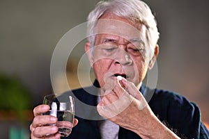 Asian senior man taking pills at home