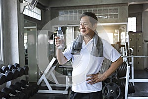 Asian senior man thirsty drinking water after exercise in fitness gym. elderly healthy lifestyle