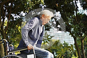 Asian senior man trying to stand up from wheel chair