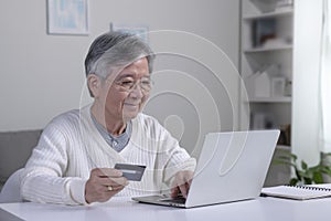 Asian senior man using Laptop and credit card payment shopping online with customer network connection via omni channel system