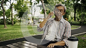 Asian senior man using smart phone, sitting alone on the bench in the park