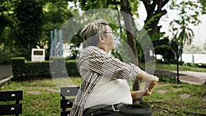 Asian senior man using smart phone, sitting alone on the bench in the park