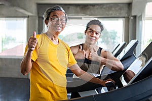 asian Senior man walking exercise on treadmill with Personal trainer workout in fitness gym and show Thumbs up . sport trainnig ,