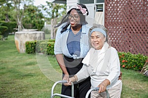 asian senior mother walk with walker and african american carer support in garden at home. old woman disabled walking and black