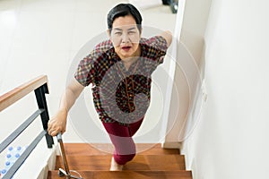 Asian senior older woman suffering from low-back lumbar pain while walking up on stair at home