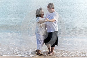 Asian senior retired couple dancing with relax happy smiling on sea beach, elder man and woman enjoying with retired vacation.