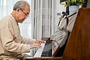 Asian senior retired man learning to play piano at home