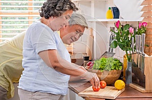 Asian senior wife slicing tomatoes on wooden cutting  board and using tablet computer to searching menu recipe.senior with technol