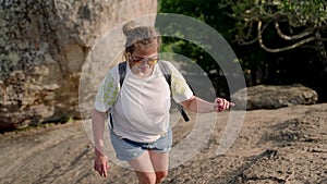 Asian senior woman with backpack hikes up mountain trail. Mature hiker tackles steep climb in morning, shows