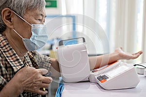 Asian senior woman check blood pressure with digital blood pressure gauge old elderly patient wear medical mask use automated