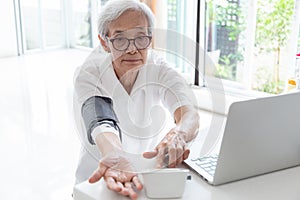 Asian senior woman checking blood pressure at home, elderly people check health using a blood pressure monitor, checking patients