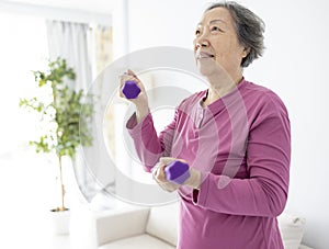 Asian senior woman doing exercises with dumbbells indoors