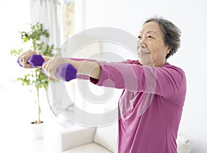 Asian senior woman doing exercises with dumbbells indoors