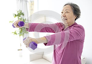 Asian senior woman doing exercises with dumbbells indoors