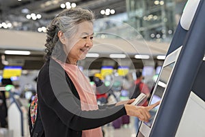 asian senior woman doing self check in at self service check in machine or KIOSK at the airport