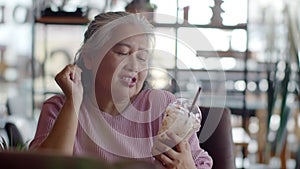 Asian senior woman drinking ice chocolate happily in coffee shop