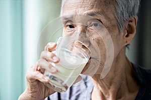 Asian senior woman drinking warm fresh milk from glass in the morning at home,old elderly eat foods that are beneficial to the photo