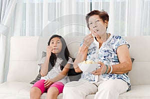 Asian senior woman eating popcorn with her grandchild