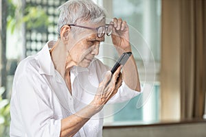 Asian senior woman with eye glasses,try to read messages,gaze at the small text on mobile phone,age related macular degeneration, photo