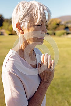 Asian senior woman with eyes closed meditating in prayer position in yard against clear sky