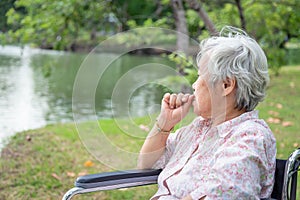 Asian senior woman feeling stressed,worried female bites finger nails in wheelchair outdoor park,elderly people with nervous